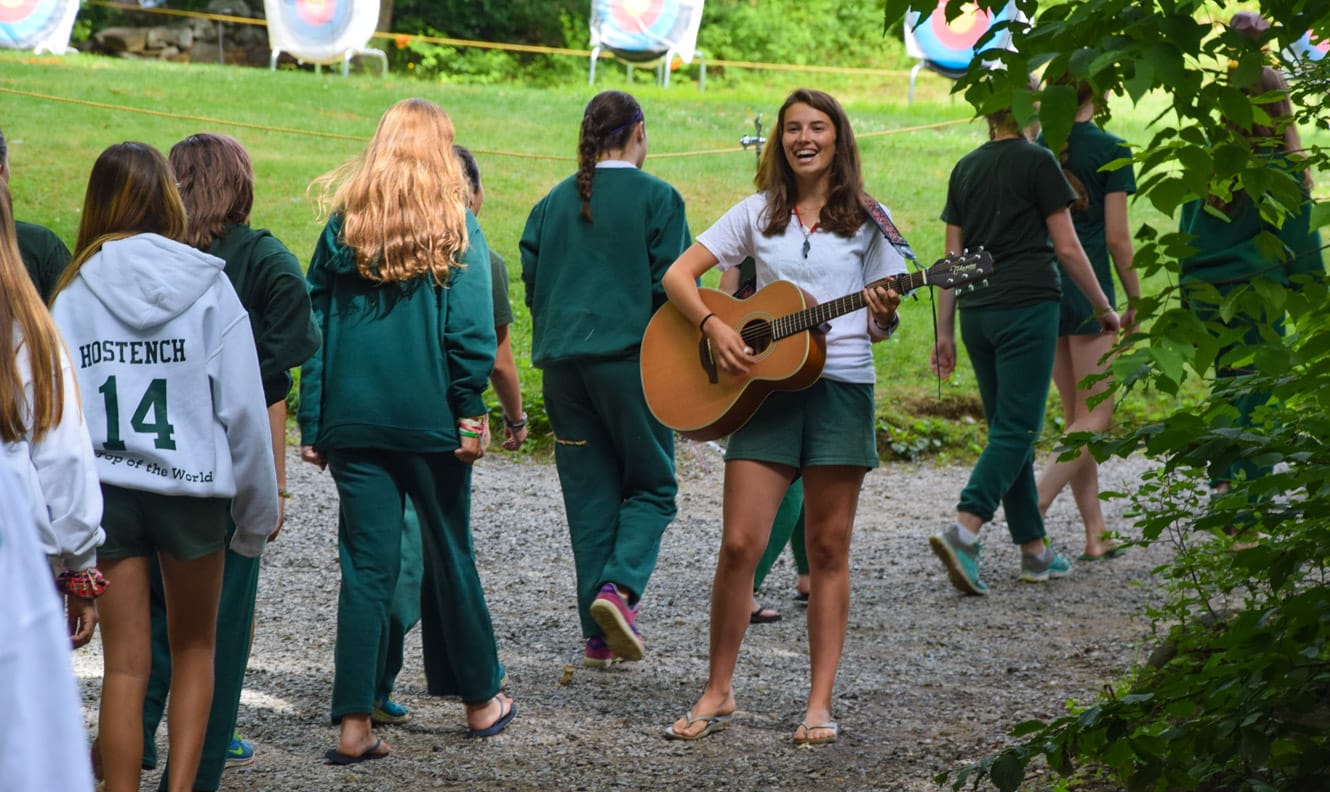 Staff playing guitar for campers walking by