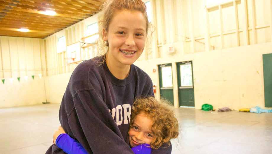 Young camper hugging staff